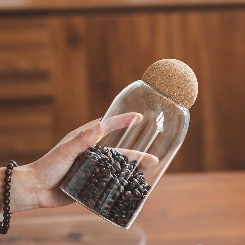 bocal en verre transparent avec bouchon de liège rempli de grains de café tenue à la main