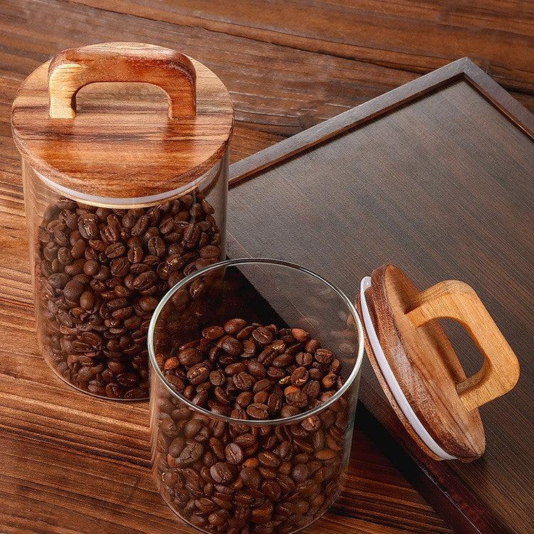 Bocal en verre transparent avec couvercle en bois à anse, rempli de grains de café, design pratique et naturel pour rangement cuisine.