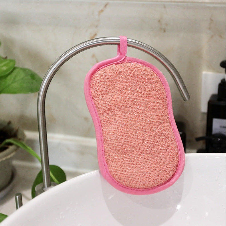 Éponge de nettoyage rose réutilisable et lavable, certifiée Oeko-Tex, suspendue au robinet de la cuisine pour un nettoyage écologique.