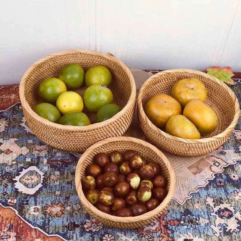 Trois paniers à fruit en rotin tressé naturel contenant des fruits variés posés sur une surface colorée.