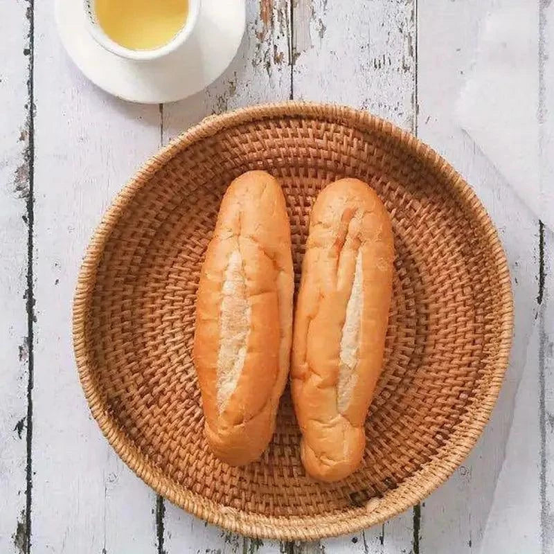Panier à fruit en rotin tressé naturel avec deux petits pains sur fond bois blanc vieilli