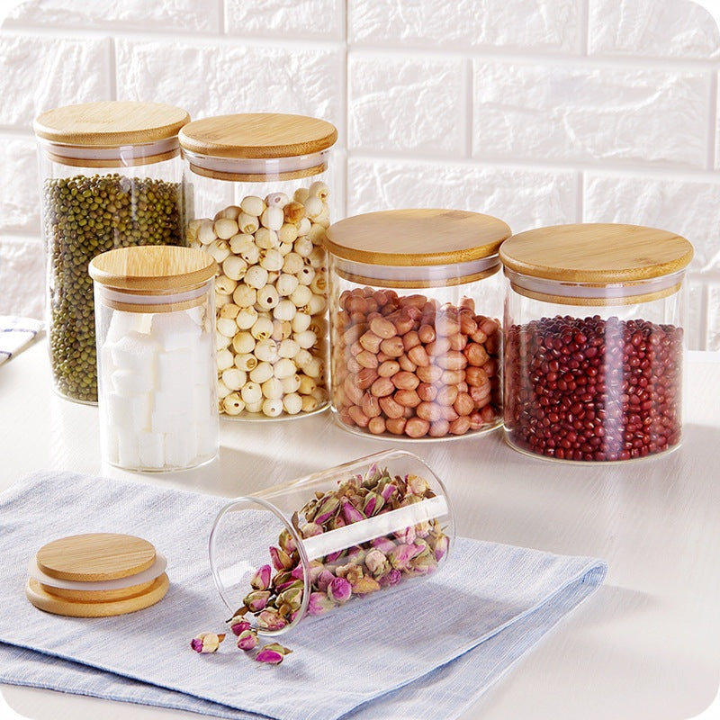 Ensemble de 5 bocaux en verre avec couvercles hermétiques en bambou remplis de divers aliments secs sur un comptoir de cuisine avec dosseret carrelé.