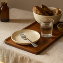 Plateau rectangulaire en bois naturel avec assiette, verre d'eau et bol de pain sur table beige.