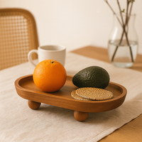 Plateau de présentation en bois naturel avec pieds ronds, orné d’une orange, d’un avocat et d’un dessous de verre en osier sur une table.