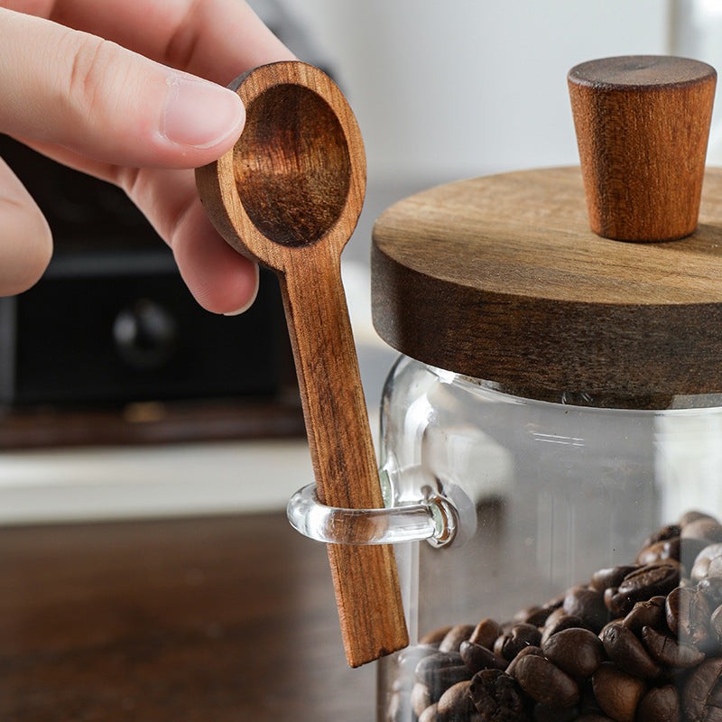 Pot en verre transparent avec couvercle et cuillère en bois pour épices ou café sur plan de travail de cuisine