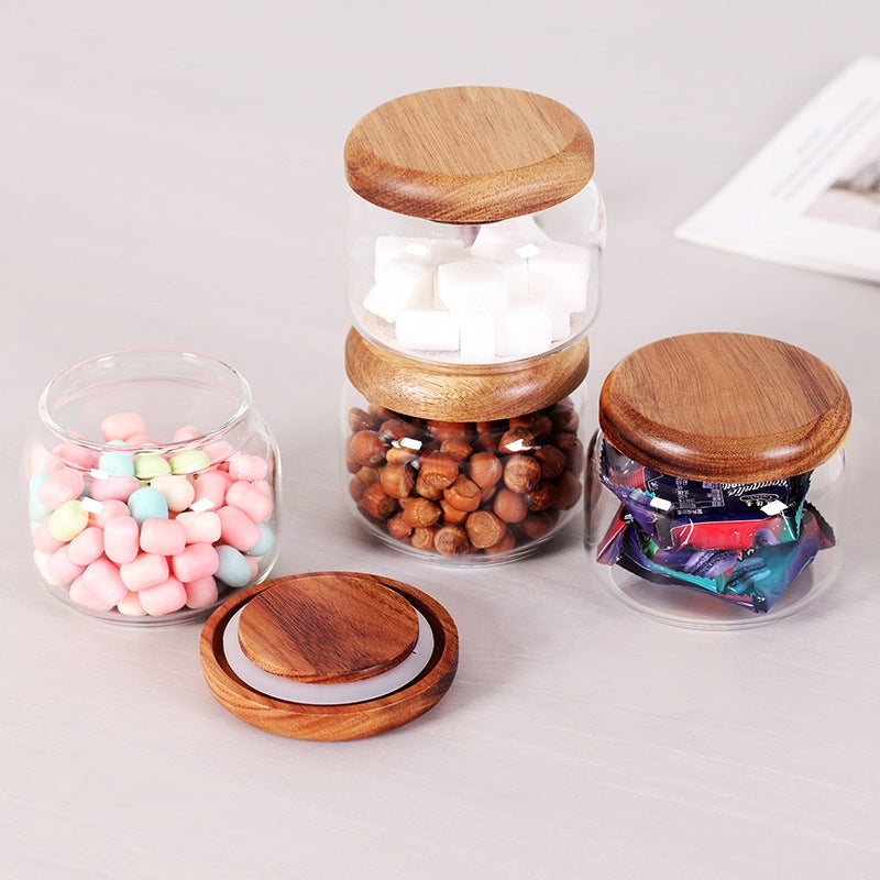 Ensemble de bocaux en verre transparent avec couvercles en bois d'acacia contenant des guimauves, des noisettes, des morceaux de sucre et des bonbons.