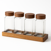 Set of 4 clear glass spice jars with wooden lids on a wooden base for kitchen organization