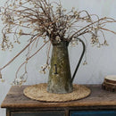 Handwoven round rattan pot mat heat insulation placemat with vintage metal pitcher and dried flowers on wooden table