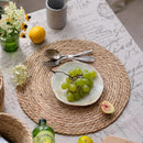 Round handwoven rattan pot mat placemat with green grapes and cutlery on table