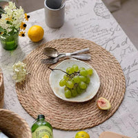 Round handwoven rattan pot mat placemat with green grapes and cutlery on table